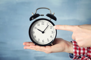 Woman holding vintage alarm clock on color background