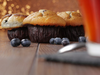 Blueberry muffins on a wooden table with blueberries, glittery background, cup of tea out of focus in foreground.