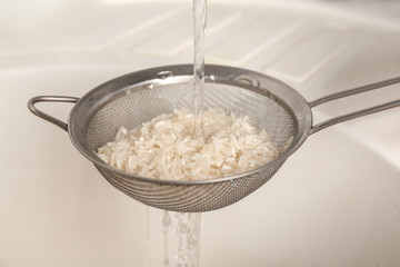 Woman rinsing rice in sifter under running water