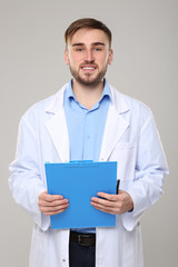 Handsome doctor with blue clipboard on light background