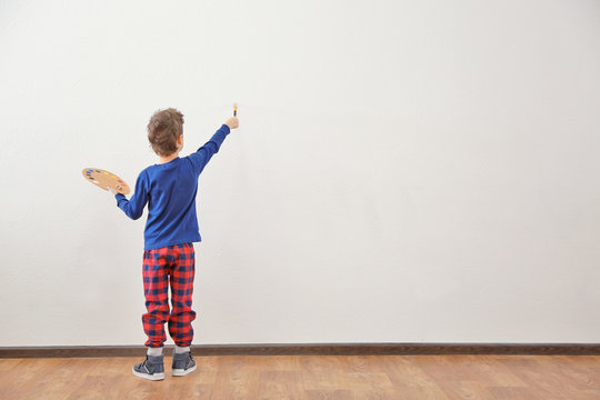 Cute little boy painting on wall in empty room