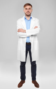 Handsome doctor with crossed hands on light background