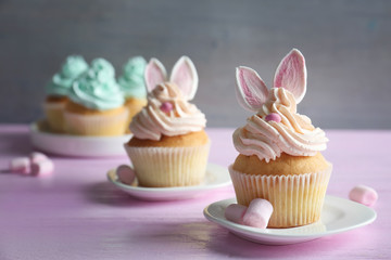 Tasty Easter cupcakes on pink wooden table against grey background