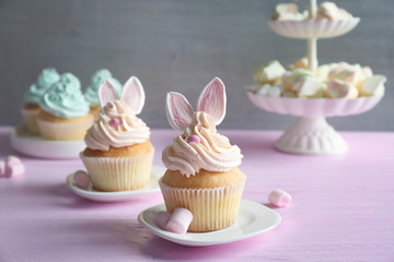 Tasty Easter cupcakes on pink wooden table against grey background