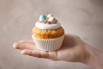 Female hand carrying delicious Easter cupcake on grey background