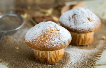Muffins powdered by sugar on jute and white wooden background.