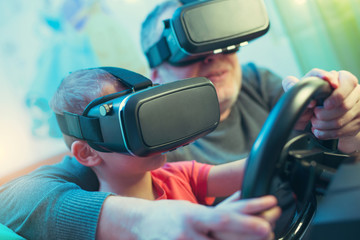 Father and son in virtual reality glasses playing video game with racing wheels at home
