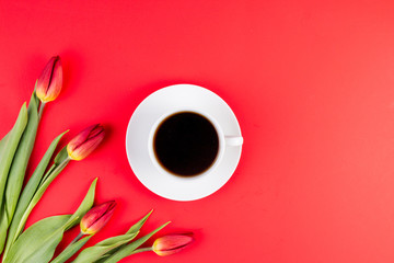 Tulips and cup of coffee on red background. Top view
