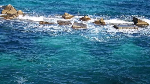 Sea turquoise waves crushing on boulders in the mediterranean sea, next to Syracuse, Sicilia
