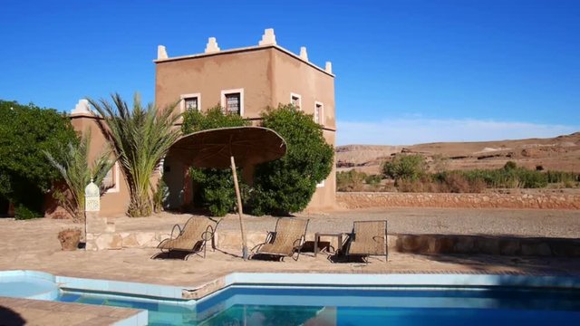View from a Riad in Ouarzazate over the swimming pool with the sun, with the desert in the background