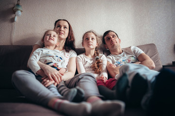 The family is sitting on the couch and watching TV