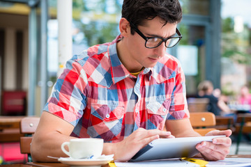 Junger Mann trinkt Kaffee in Straßencafe und liest die Nachrichten auf einem Tablet PC