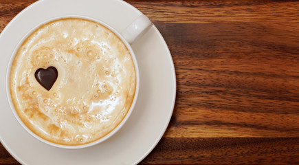 Cappuccino. A cup of coffee with a chocolate heart. Wooden background. Close-up. View from above