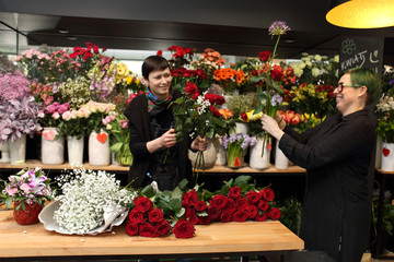 Dwie uśmiechnięte kobiety w kwiaciarni robią bukiety z kwiatów ciętych. - obrazy, fototapety, plakaty