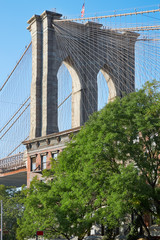 Brooklyn Bridge pillar and green trees in New York, sunny day