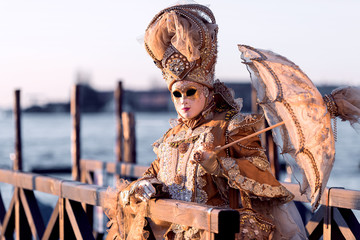Precious golden costume with little umbrella on a jetty at Carnival in Venice