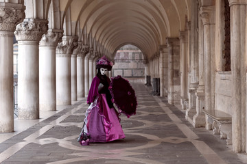 Lonely lady in violet costume in the colonnade of Doge's Palace at Carnival in Venice
