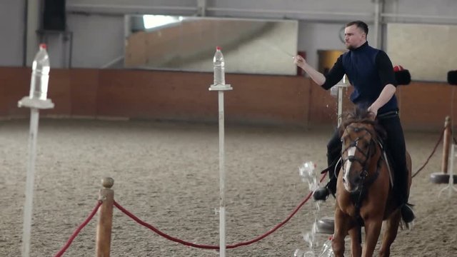 Young man riding his horse and swinging his sword. A Cossack horseman cuts through a Water Bottle.