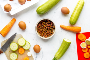 dry food for dogs, eggs and vegetables on kitchen background top view