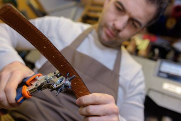 Man punching hole in leather belt