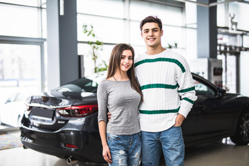 Smiling couple standing in front of a car at new car showroom