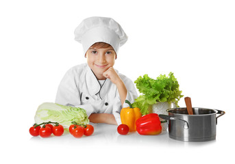 Cute boy in chef uniform with vegetables and saucepan on white background