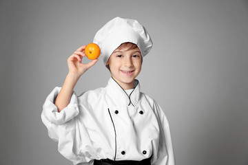 Cute boy in chef uniform on color background