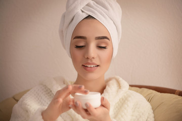 Beautiful young woman applying cream onto skin in spa salon