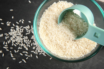 Glass bowl and scoop with rice on dark background