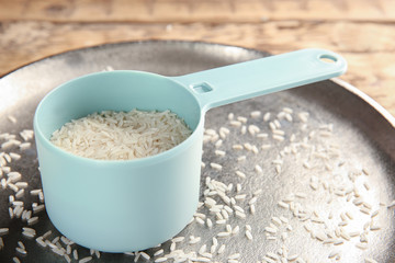 Tray with rice in scoop on wooden table