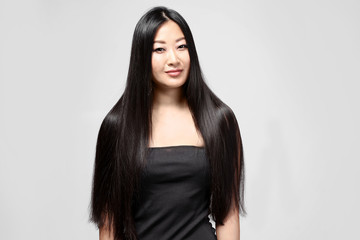 Naklejka premium Beautiful Asian woman with long straight hair on light background