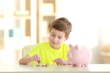 Little boy saving coins in piggy bank at home