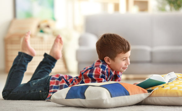 Little boy reading book on floor with pillows indoors