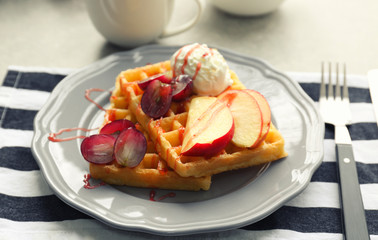 Tasty waffles with delicious fruits, ice-cream and syrup on grey plate