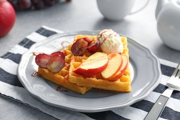 Tasty waffles with delicious fruits, ice-cream and syrup on grey plate