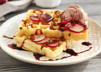 Tasty waffles with delicious grape, ice-cream and syrup on white plate
