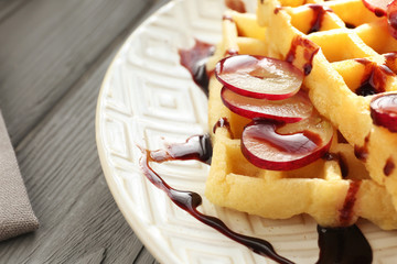 Tasty waffles with delicious grape and syrup on white plate, close up