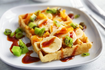 Delicious waffle with fruits and syrup on white plate