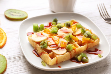 Delicious waffle with fruits and syrup on white plate