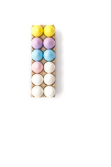 Seven Easter eggs dyed yellow, lavender, blue and pink with five white hard boiled hen's eggs in a tan cardboard carton from above against a white background.
