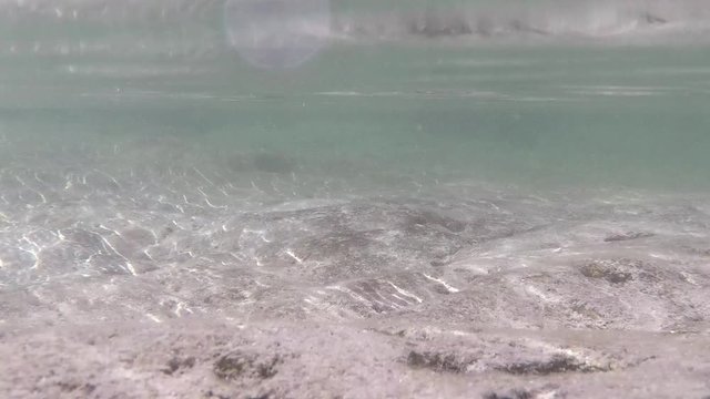 Slow motion wave underwater light reflection on the sunny rocky seabed. 