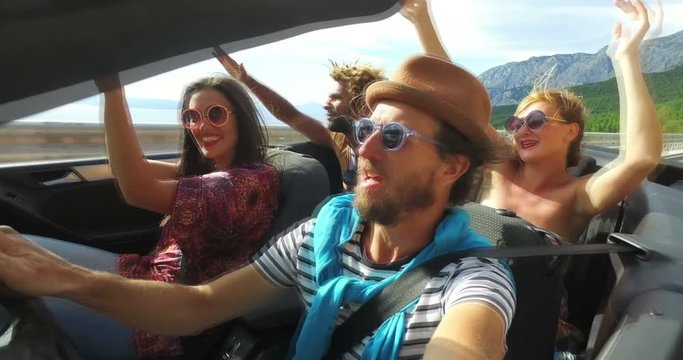 Four young hipster friends having fun riding in convertible