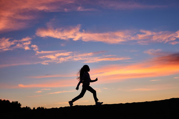 A silhouette of a running girl on sunset sky background