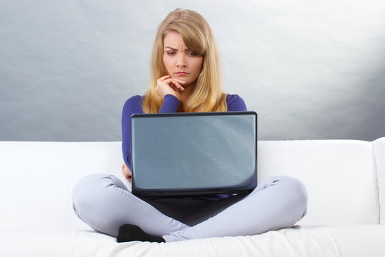 Surprised woman sitting on sofa and looking at laptop, modern technology