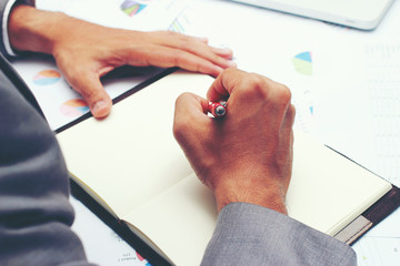 Businessman writing a business report on blank notebook with red pen on desk office. .Business concept: