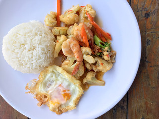 stir-fry vegetables with bean curd and shrimp in white dish with rice and fried egg on wooden background. Thai style Food.
