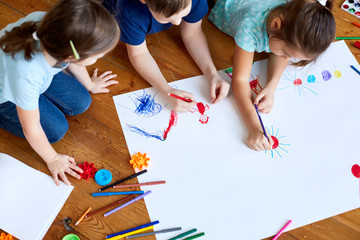 children lying on the floor and drawing. Children draw on a large sheet of paper