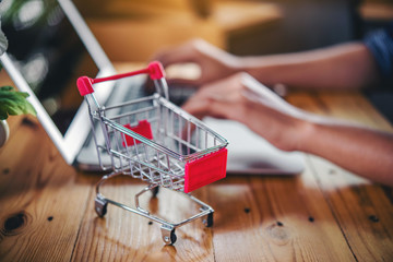 Red shopping cart and laptop on wooden table,shopping online concept.