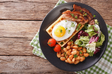 Delicious breakfast: fried egg, waffles, bacon, beans and salad close-up. horizontal top view