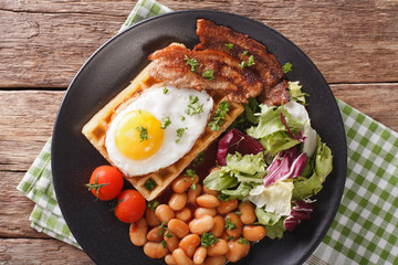 Breakfast with fried egg, waffles, bacon, mix lettuce and beans close-up. horizontal top view